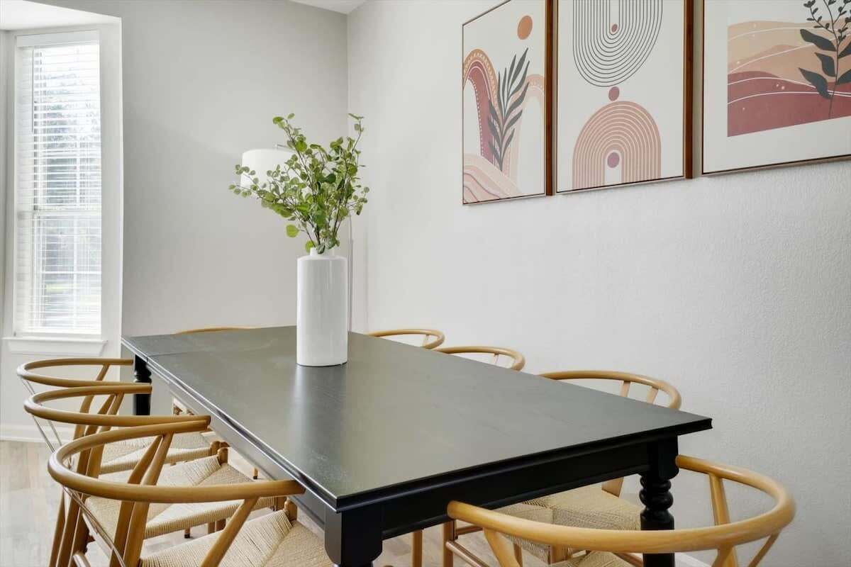 A dining area with a black table, wicker chairs, a white vase with a plant, and abstract wall art.