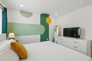 A modern hotel room with a bed, a TV, a dresser, and a lamp. - Heart of Dallas in Knox Henderson Sleeps 4 (Dallas)