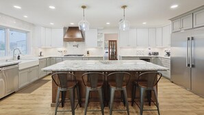A modern kitchen with a large island, bar stools, stainless steel appliances, and pendant lighting. - Lone Star Getaway - 5bd/3ba w Game Room & Backyard (McKinney)