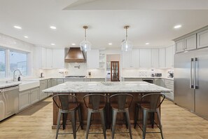 A modern kitchen with a large island, bar stools, stainless steel appliances, and pendant lighting. - Lone Star Getaway - 5bd/3ba w Game Room & Backyard (McKinney)