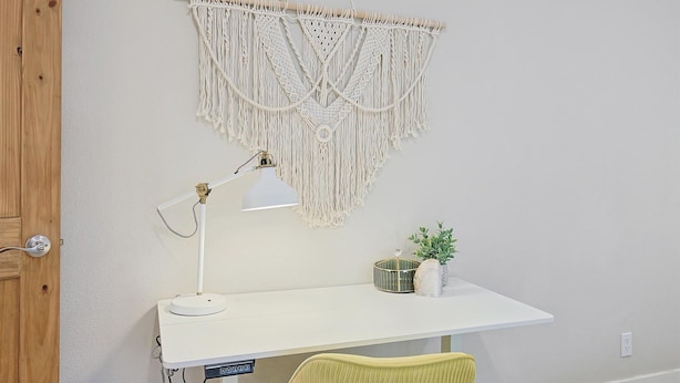 A white desk with a macrame wall hanging, a desk lamp, a small plant, and a decorative item on the desk. - Lone Star Getaway - 5bd/3ba w Game Room & Backyard (McKinney)