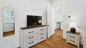 Et soveværelse med fjernsyn, et natbord med lampe, et klædeskab og en dør til et andet rum.