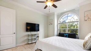 A bedroom with a bed, a ceiling fan, a TV, a large window, and a door. - Peace River Waterfront Luxury Living - 5-bd w Pool (Punta Gorda)