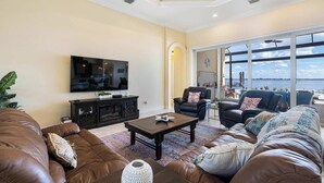 A living room with leather sofas, a coffee table, a TV, and a large window with a view. - Peace River Waterfront Luxury Living - 5-bd w Pool (Punta Gorda)