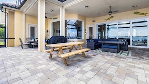 A covered patio with a wooden picnic table, outdoor seating, and a view through large windows. - Peace River Waterfront Luxury Living - 5-bd w Pool (Punta Gorda)