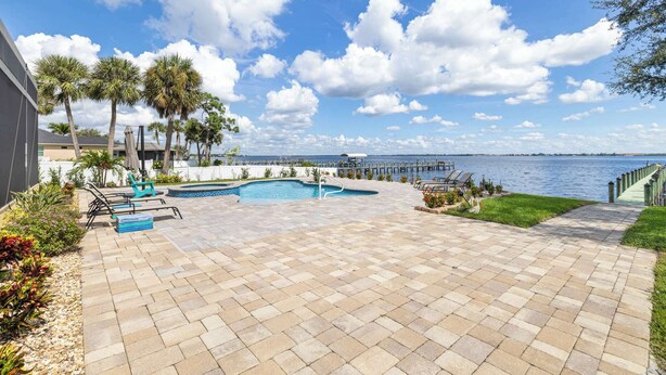 A swimming pool with lounge chairs, palm trees, and a view of the water. - Peace River Waterfront Luxury Living - 5-bd w Pool (Punta Gorda)