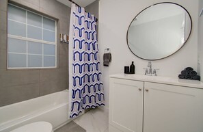 A bathroom with a bathtub, a shower curtain, a sink with a mirror, and a toilet. - Heart of Houston - 2-bd/1-ba With Grill (Houston)