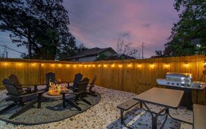 An outdoor patio area with a wooden fence, a grill, and seating around a fire pit. - Heart of Houston - 2-bd/1-ba With Grill (Houston)