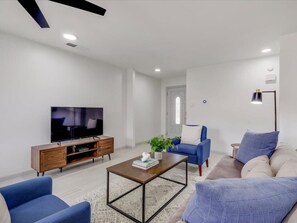 Ein modernes Wohnzimmer mit Flachbildfernseher, einer Holz-Unterhaltungseinheit, einem Couchtisch, einer Couch und einem blauen Sessel.