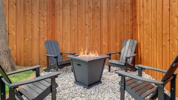 A patio area with a metal fire pit, two Adirondack chairs, and a wooden fence. - Best of Irving - Yard, Firepit, Free Parking (Irving)