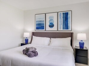 Ein Hotelzimmer mit einem großen Bett, zwei Nachttischen, einem Kopfteil und drei gerahmten Kunstwerken an der Wand.