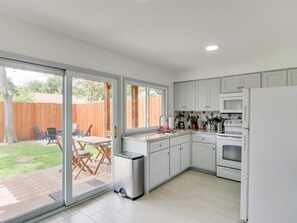 Eine moderne Küche mit weißen Schränken, einem Edelstahlherd und einem eingebauten Backofen. Ein Glastürverschluss führt auf eine Terrasse mit Gartenmöbeln.