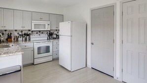 A compact kitchen with white cabinets, a microwave, a refrigerator, and an oven. - Best of Irving - Yard, Firepit, Free Parking (Irving)