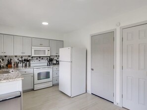 Eine Küche mit weißen Schränken, einer Mikrowelle, einem Backofen und einem Kühlschrank.