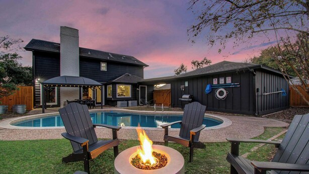 Patio trasero con piscina, mobiliario exterior y una chimenea.