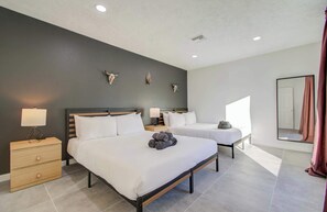 A modern hotel room with two beds, a wooden nightstand with a lamp, a mirror, and decorative skulls on the wall. - 5BD Cozy Rustic Retreat - Pool & Firepit (Houston)