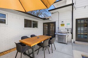Eine Terrasse im Freien mit Holztisch und -stühlen, einem Grill und einem Warnschild.