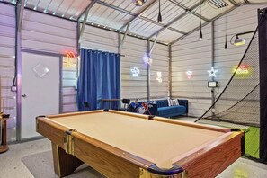 A pool table in a room with a blue couch, neon lights, and a netted area. - 5BR Near At&t Stadium Pool, Golf Sim, EV (North Richland Hills)