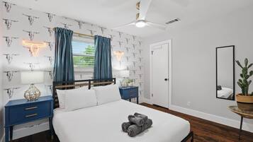 A bedroom with a bed, two nightstands, a ceiling fan, a window with curtains, a door, and a mirror.