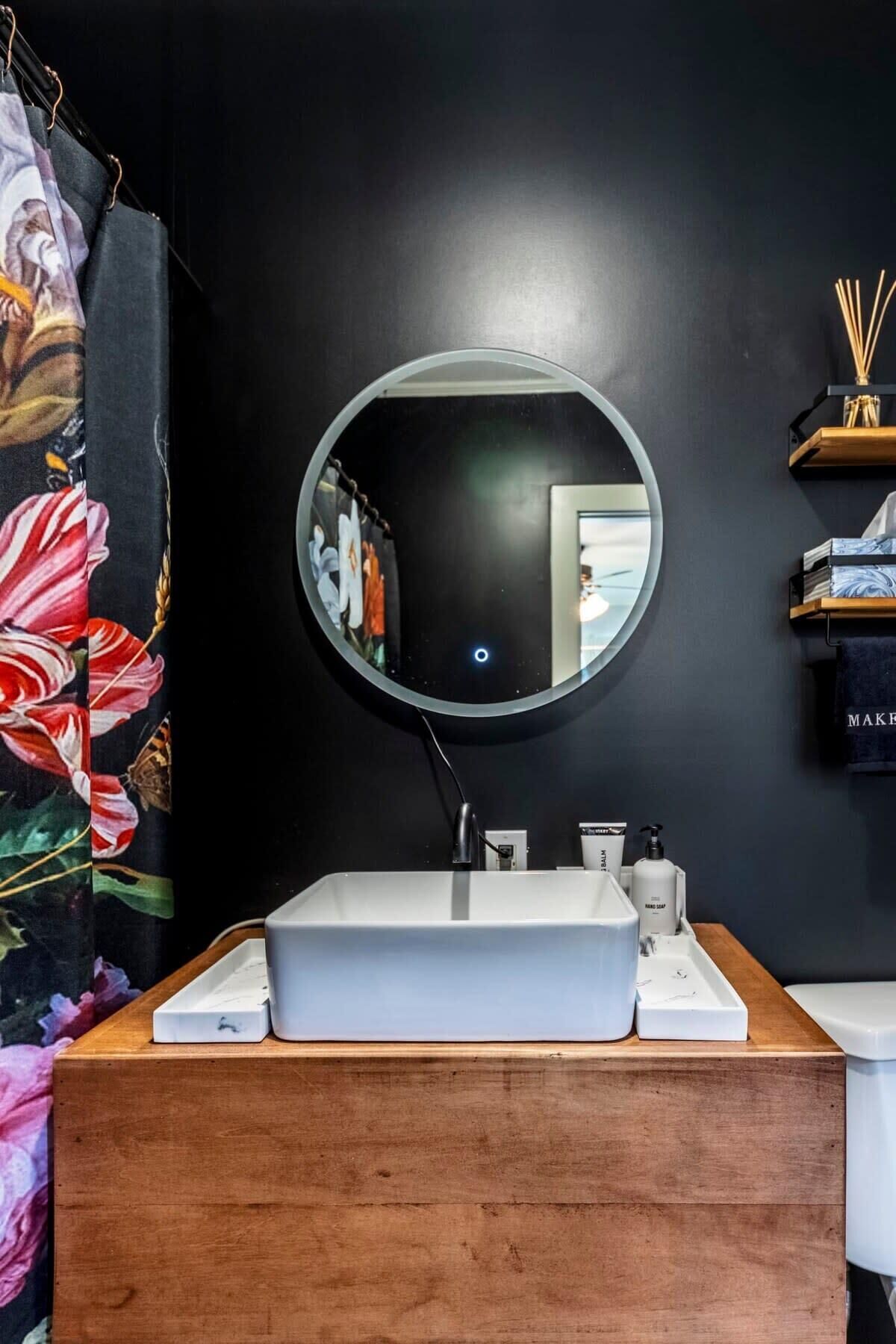 A bathroom with a wooden vanity, a round mirror, and a white sink.