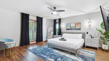 A modern bedroom with a large bed, a ceiling fan, a nightstand, a chair, and a view of the outdoors.