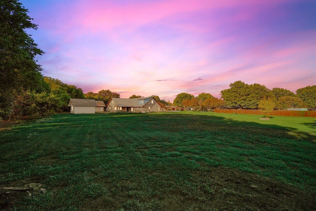 A large grassy field with a barn and a house in the background.