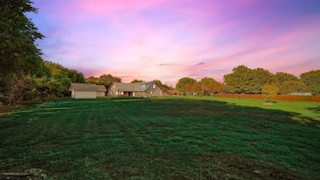 A large grassy field with a barn and a house in the background.