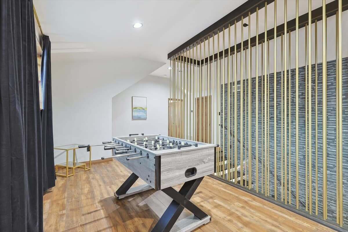 A modern room with a foosball table, wooden flooring, and a large window with vertical blinds.