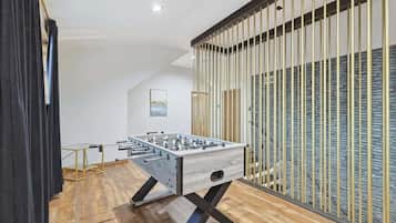 A modern room with a foosball table, wooden flooring, and a large window with vertical blinds.