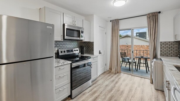 Een moderne keuken met roestvrijstalen apparatuur, witte kasten en een schuifdeur naar een terras.