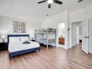A bedroom with a large bed, a bunk bed, wooden flooring, a ceiling fan, and a wall with framed pictures. - Modern Rustic Oasis/games/cinema/utd/plano/frisco (Allen)