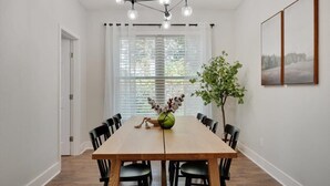 A dining room with a wooden table and black chairs, a chandelier, a window with blinds, and a potted plant. - Tropical Pool Oasis - 5 BR, Foosbal, Cinema (Flower Mound)