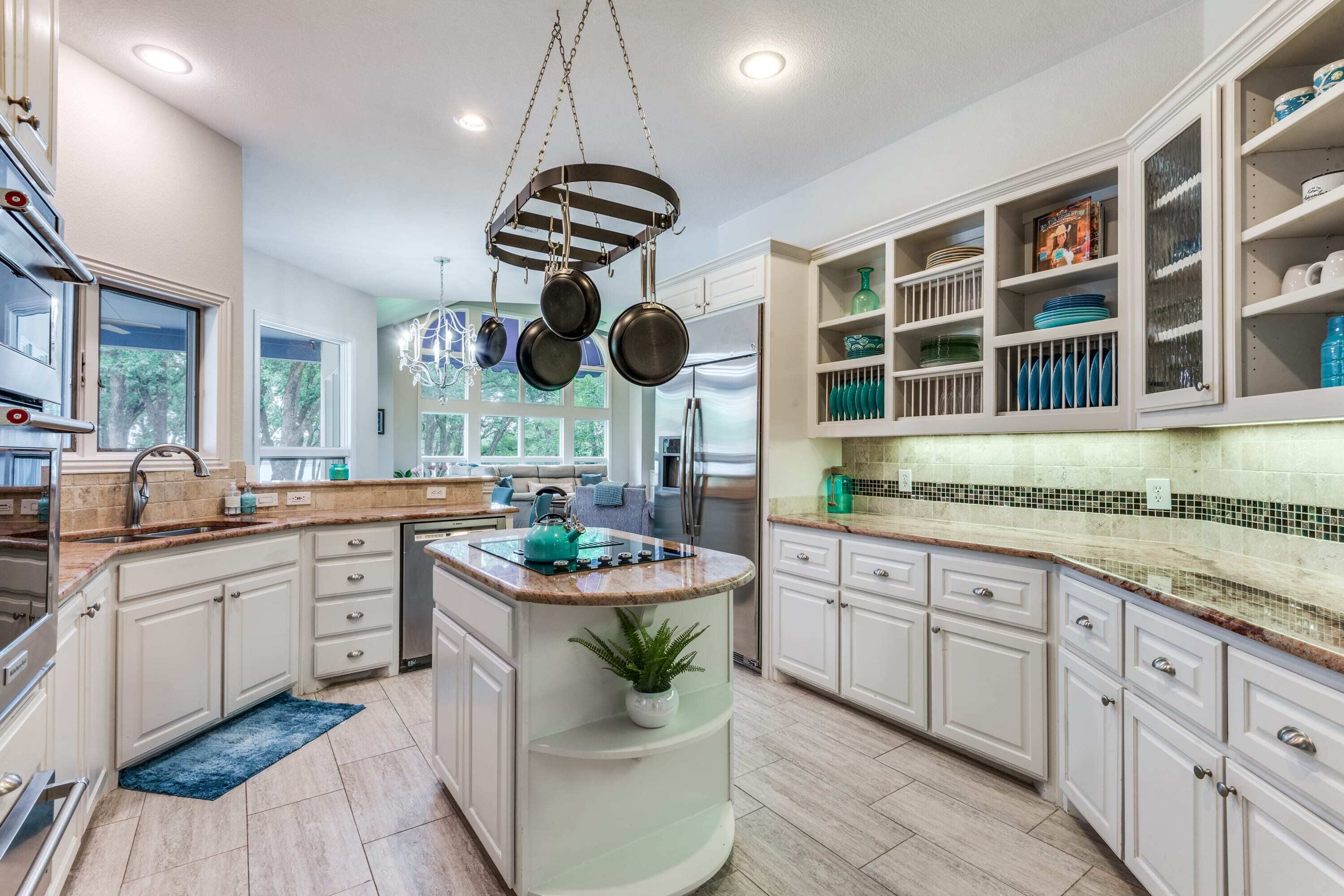 A modern kitchen with white cabinetry, a central island, and a hanging pot rack.