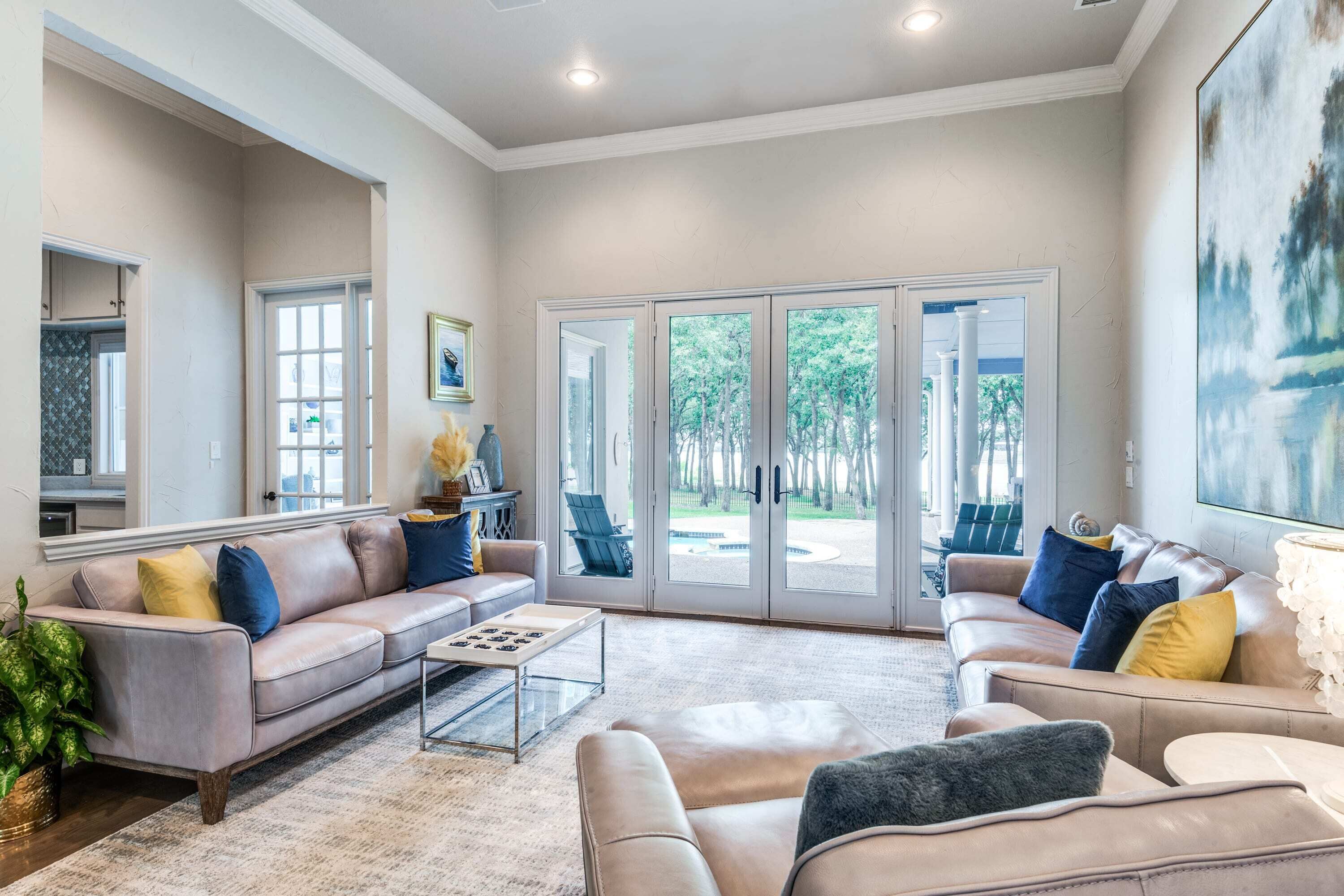 A spacious living room with a beige sofa, a coffee table, and a large window with a view of trees.