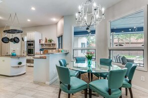 A modern kitchen with a central island, a dining area with teal chairs, and a chandelier. - Lakefront Oasis Home w/ Pool & Sand Beach (Little Elm)