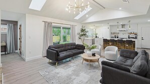 A spacious living room with a dark grey sofa, a round coffee table, and a modern chandelier. - 3-bd Backyard Oasis w Pool, Patio, Firepit (Irving)