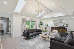 Ein geräumiges Wohnzimmer mit einem dunkelgrauen Sofa, einem runden Couchtisch und einem modernen Kronleuchter.