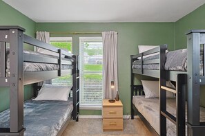 Ein Zimmer mit Etagenbetten, einem Fenster mit Vorhängen und einem Nachttisch mit Lampe.