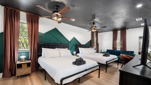 Quarto de hotel com duas camas, uma escrivaninha, televisão e ventoinhas de teto.