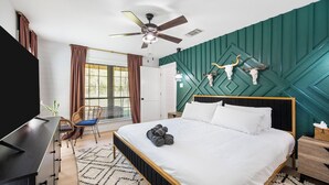 A modern hotel room with a bed, a desk, a chair, a ceiling fan, and a window with curtains. - Tranquil Country Escape, 4 Bedrooms, Pond, Firepit (Greenville)