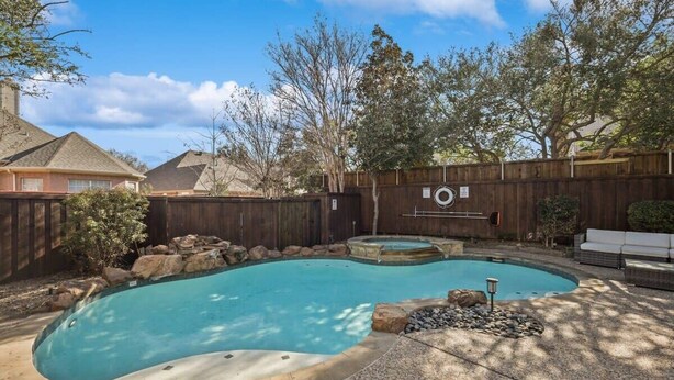 A backyard with a swimming pool, a wooden fence, and a stone border. - Dream Vacay in Central Plano - Pool & Grill (Plano)