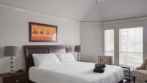 A neatly made bed with white linens, two bedside lamps, a framed artwork above the bed, and a chair by the window. - Dream Vacay in Central Plano - Pool & Grill (Plano)