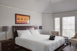 Ein Hotelzimmer mit einem großen Bett, zwei Nachttischlampen, einem Sessel und einem Fenster mit Jalousien.