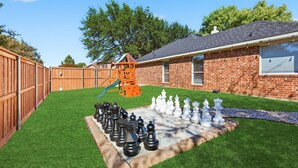 A backyard with a brick house, a wooden fence, a play structure, and a chessboard. - 4-bd/2-ba With Backyard Pool Retreat + Game room (Lancaster)