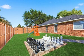 A backyard with a play structure, a brick house, and a chessboard. - 4-bd/2-ba With Backyard Pool Retreat + Game room (Lancaster)