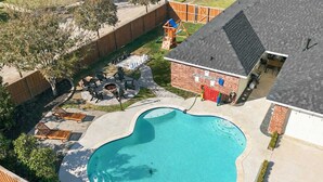 A backyard with a swimming pool, a brick building, and a fenced area with outdoor furniture. - 4-bd/2-ba With Backyard Pool Retreat + Game room (Lancaster)
