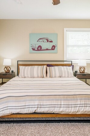 Un dormitorio con cama, dos mesitas de noche, un reloj de pared, una ventana con persianas y una ilustración de un coche en la pared.