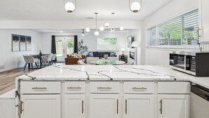 A modern kitchen with a large island, white cabinetry, and a built-in microwave. - Bright Modern Home 3br, 2ba, Fenced backyard (Irving)
