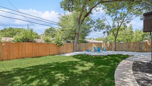 A backyard with a wooden fence, a lawn, and a patio area with blue chairs. - Bright Modern Home 3br, 2ba, Fenced backyard (Irving)