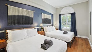 Een hotelkamer met twee bedden, een groot raam met gordijnen, een plafondventilator en een kunstwerk aan de muur.